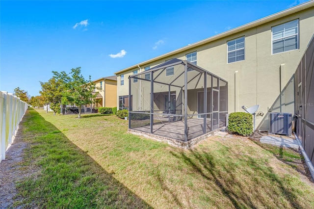 rear view of property with stucco siding, central air condition unit, a lawn, glass enclosure, and fence