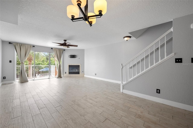 unfurnished living room with stairway, a glass covered fireplace, wood finished floors, baseboards, and ceiling fan with notable chandelier