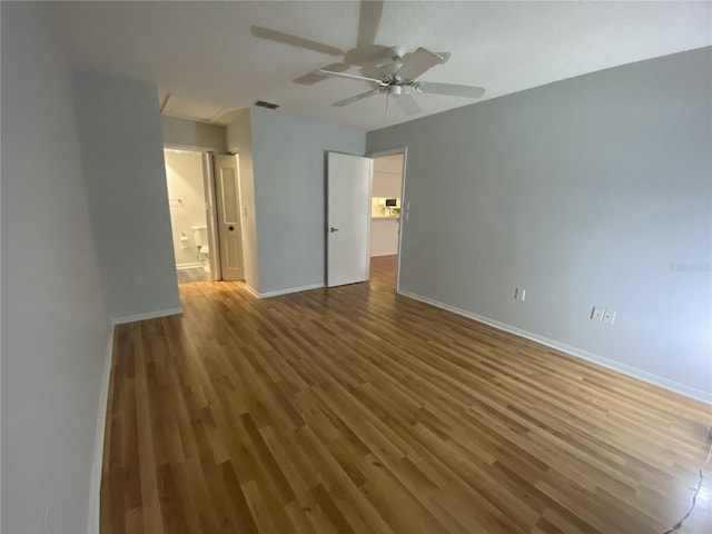 unfurnished bedroom featuring ensuite bathroom, wood finished floors, a ceiling fan, visible vents, and baseboards