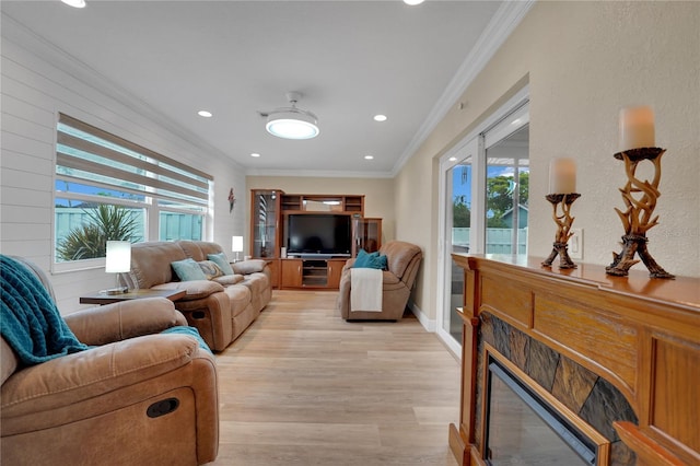 living room featuring light wood-style flooring, recessed lighting, baseboards, a glass covered fireplace, and crown molding