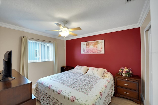 bedroom with a ceiling fan, an accent wall, crown molding, and wood finished floors