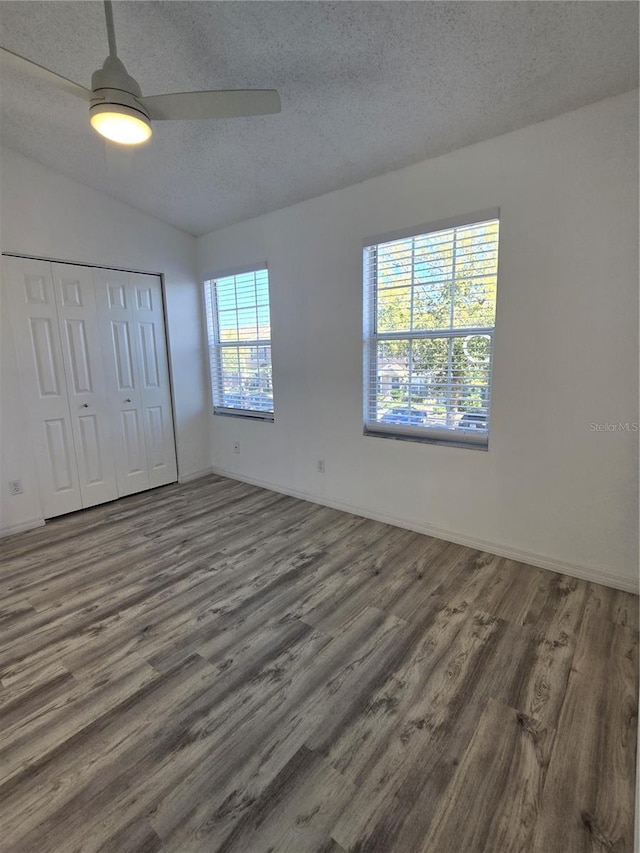 unfurnished bedroom with lofted ceiling, ceiling fan, a textured ceiling, wood finished floors, and a closet