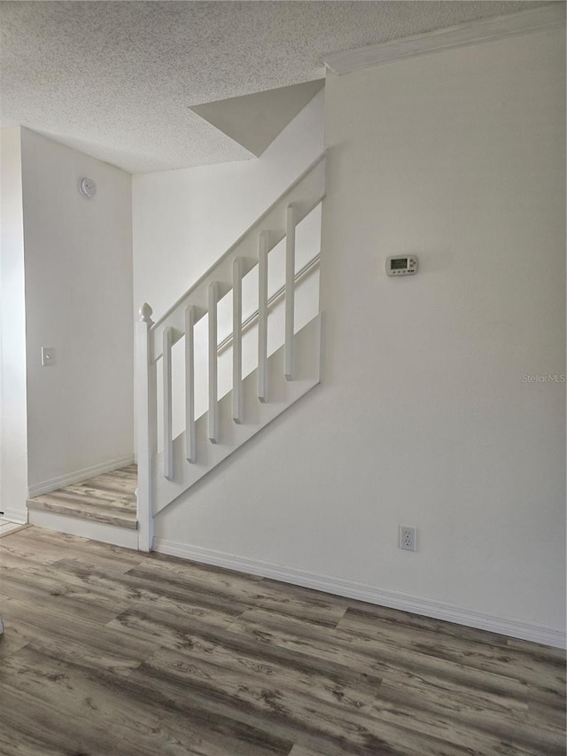 staircase with baseboards, a textured ceiling, and wood finished floors