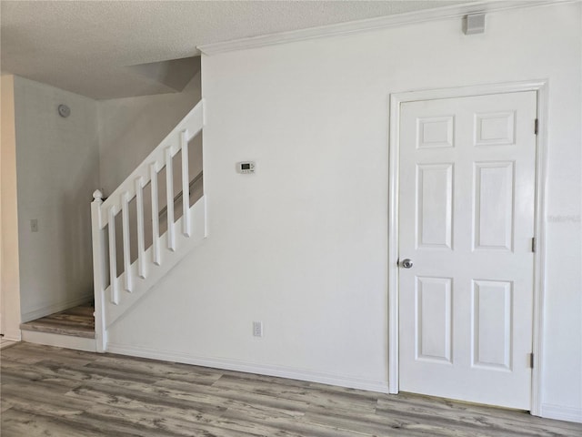 staircase with a textured ceiling, baseboards, and wood finished floors