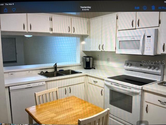 kitchen featuring white cabinets, white appliances, light countertops, and a sink