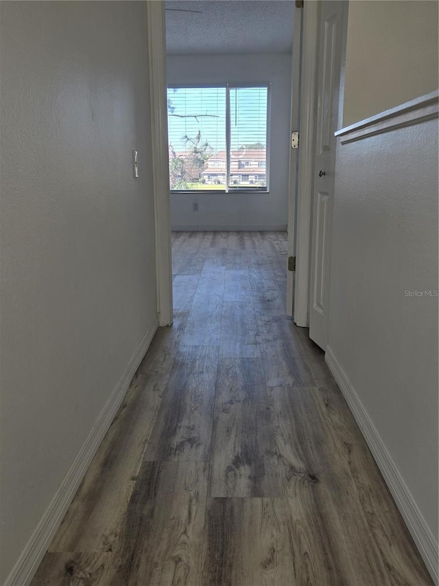 hallway featuring a textured ceiling, baseboards, and wood finished floors