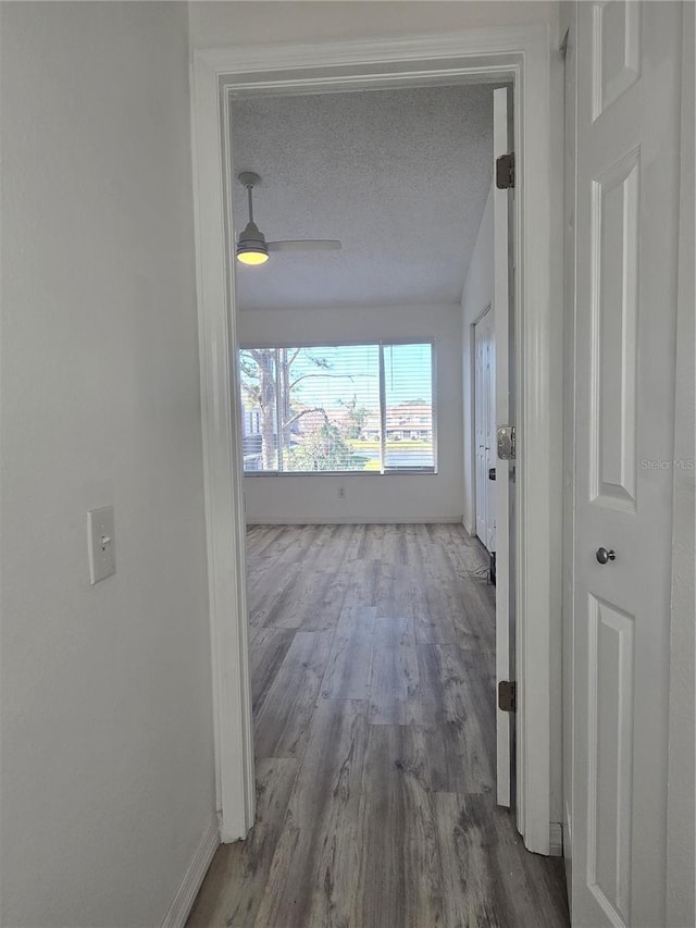 hallway with a textured ceiling, wood finished floors, and baseboards