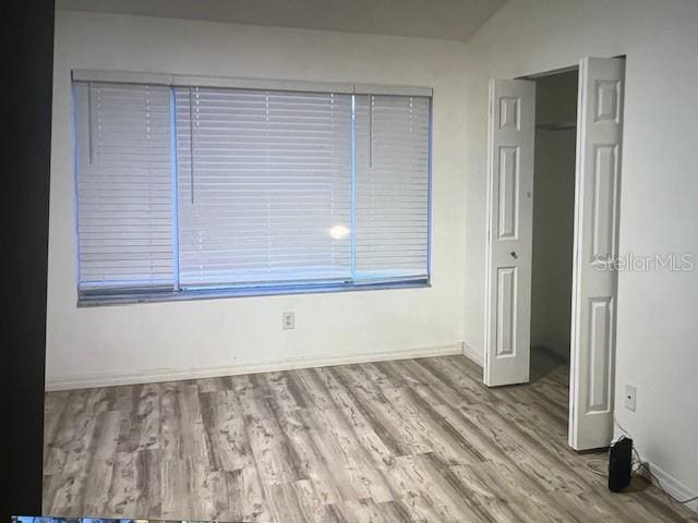 spare room featuring baseboards, vaulted ceiling, and wood finished floors