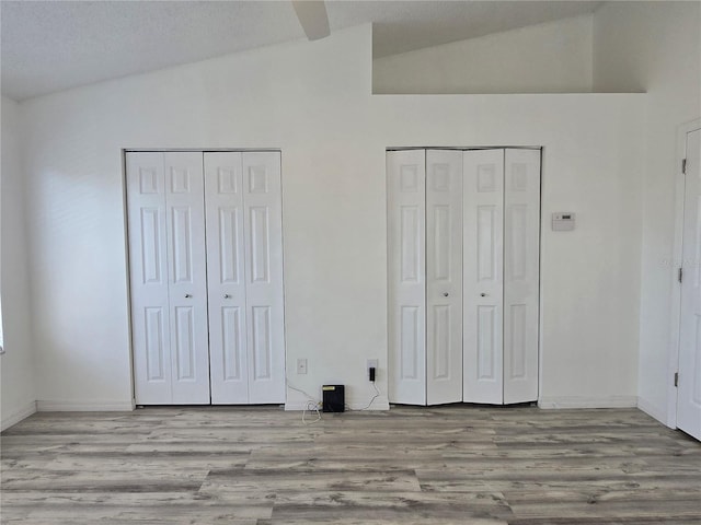 unfurnished bedroom featuring vaulted ceiling, wood finished floors, two closets, and baseboards