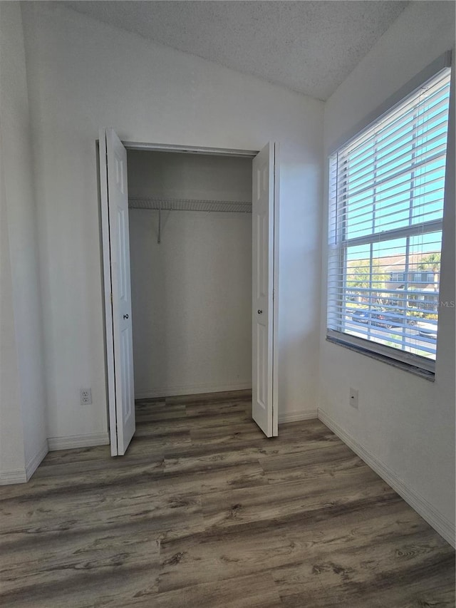 unfurnished bedroom with a closet, a textured ceiling, baseboards, and wood finished floors