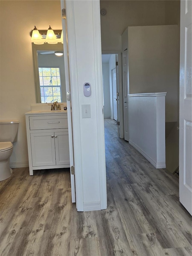 bathroom featuring toilet, baseboards, wood finished floors, and vanity