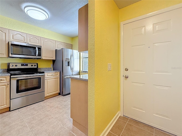 kitchen with light tile patterned floors, appliances with stainless steel finishes, and a textured wall