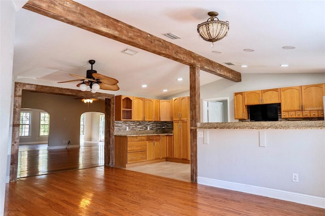 kitchen featuring visible vents, vaulted ceiling with beams, arched walkways, light wood-style floors, and tasteful backsplash