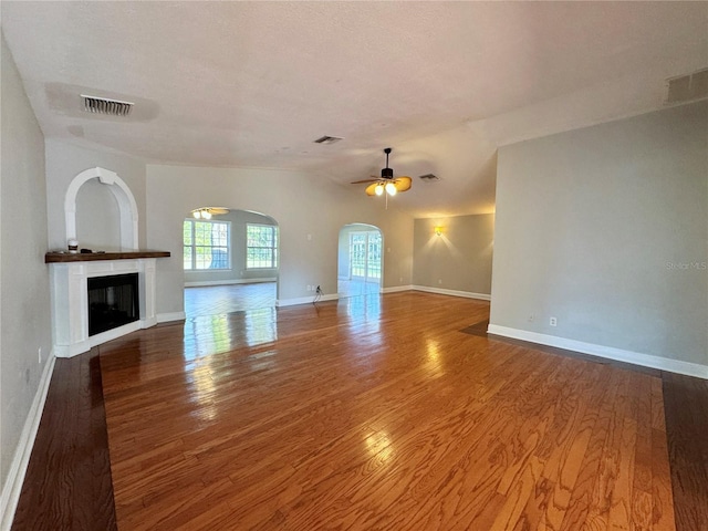 unfurnished living room with arched walkways, visible vents, wood finished floors, and a glass covered fireplace