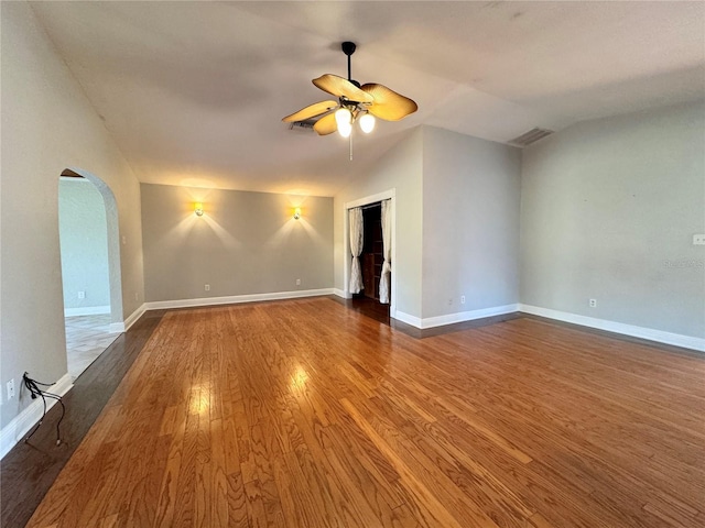 spare room featuring baseboards, vaulted ceiling, wood finished floors, arched walkways, and a ceiling fan