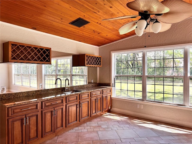 kitchen featuring wood ceiling, vaulted ceiling, brown cabinets, a textured wall, and a sink