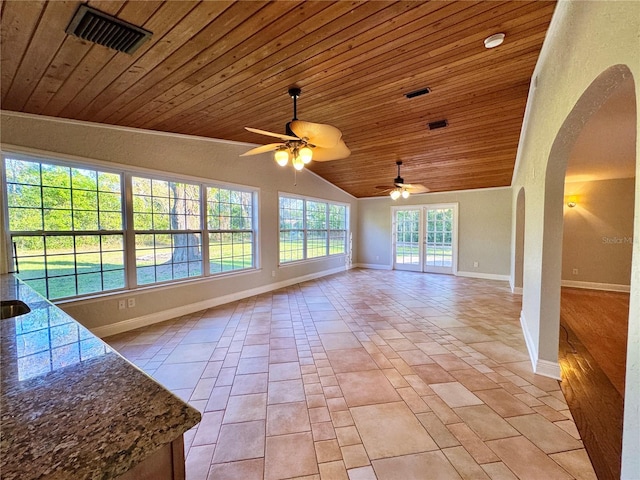 unfurnished living room with visible vents, arched walkways, light tile patterned flooring, baseboards, and vaulted ceiling