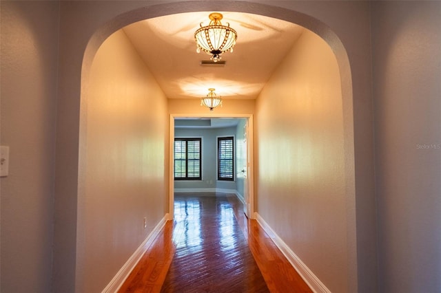 corridor featuring visible vents, dark wood-style floors, baseboards, and arched walkways