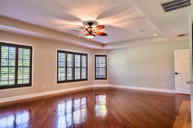 spare room with visible vents, baseboards, hardwood / wood-style floors, a textured ceiling, and a raised ceiling