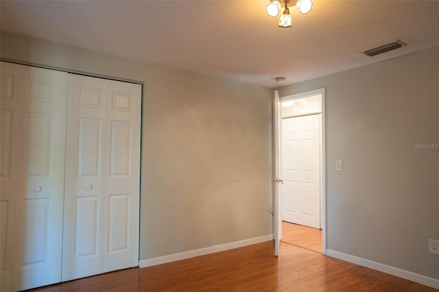 unfurnished bedroom with a closet, visible vents, baseboards, and wood finished floors