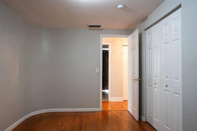 corridor featuring visible vents, a textured ceiling, wood finished floors, arched walkways, and baseboards