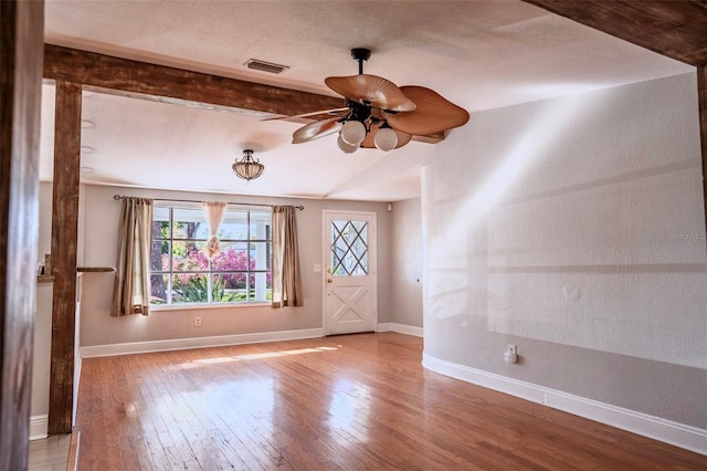 interior space with hardwood / wood-style floors, a ceiling fan, baseboards, visible vents, and beamed ceiling