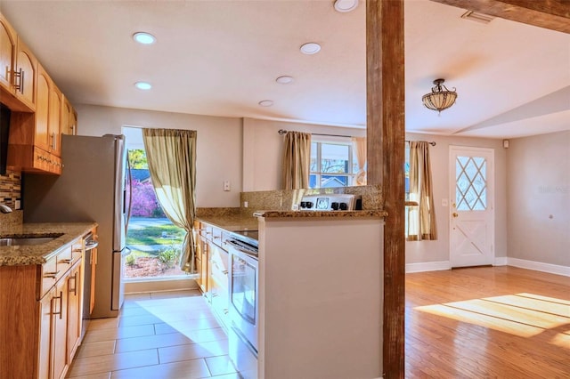 kitchen featuring light stone countertops, light wood-type flooring, stainless steel appliances, and a sink