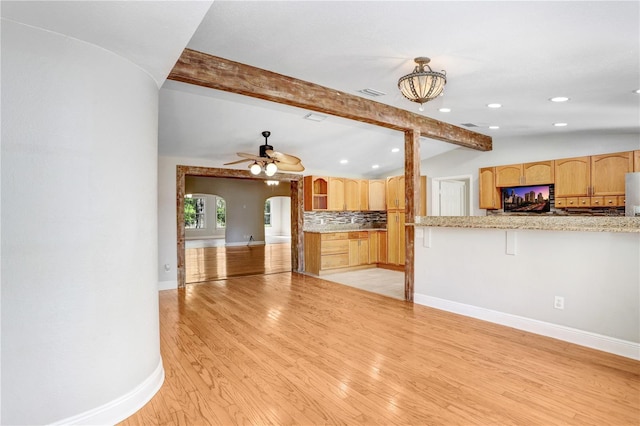 kitchen featuring vaulted ceiling with beams, baseboards, light wood-type flooring, decorative backsplash, and arched walkways