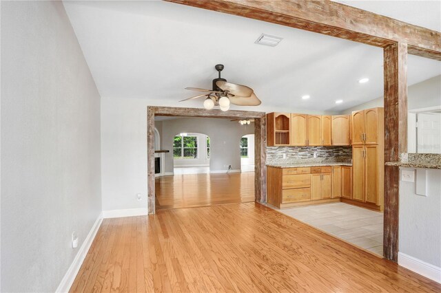 kitchen featuring visible vents, a ceiling fan, tasteful backsplash, arched walkways, and light wood finished floors