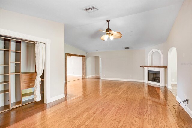unfurnished living room featuring light wood-style flooring, a ceiling fan, arched walkways, a fireplace, and vaulted ceiling