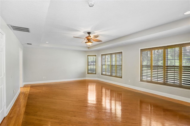 empty room with visible vents, a ceiling fan, baseboards, and wood finished floors