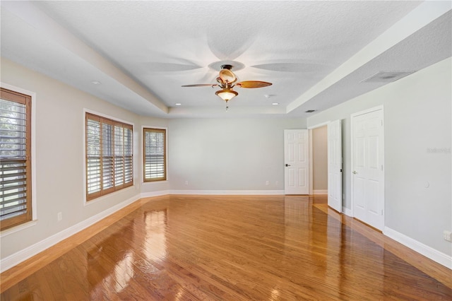 spare room with visible vents, baseboards, wood finished floors, a textured ceiling, and a raised ceiling