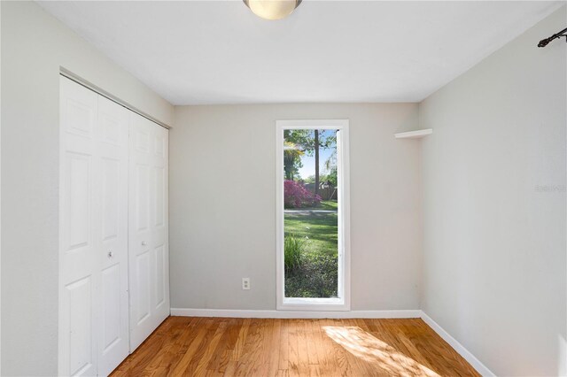 unfurnished bedroom featuring light wood-style flooring, baseboards, and a closet