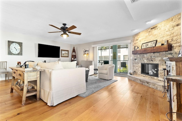 living area featuring a ceiling fan, light wood-type flooring, and a fireplace