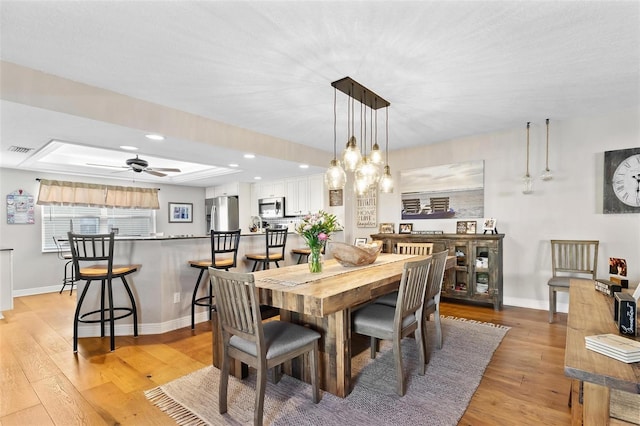 dining area with ceiling fan, light wood-style flooring, visible vents, and baseboards