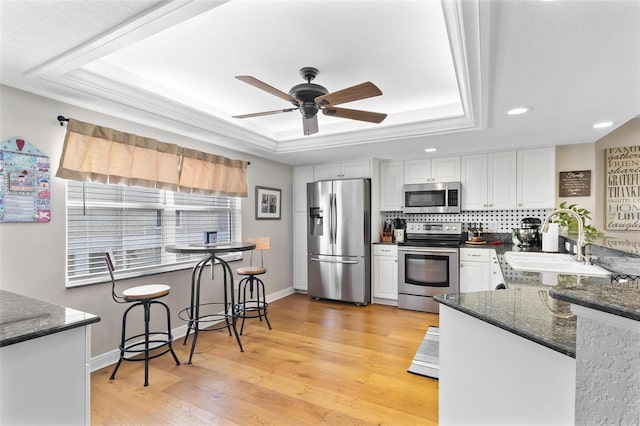 kitchen featuring stainless steel appliances, a raised ceiling, white cabinets, and a sink