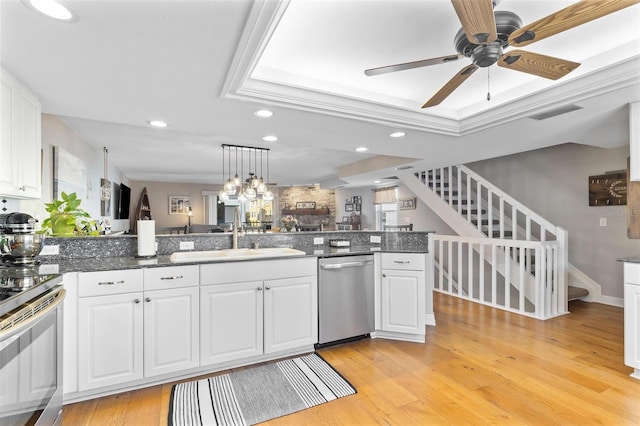 kitchen featuring a tray ceiling, stainless steel appliances, light wood-type flooring, white cabinetry, and a sink