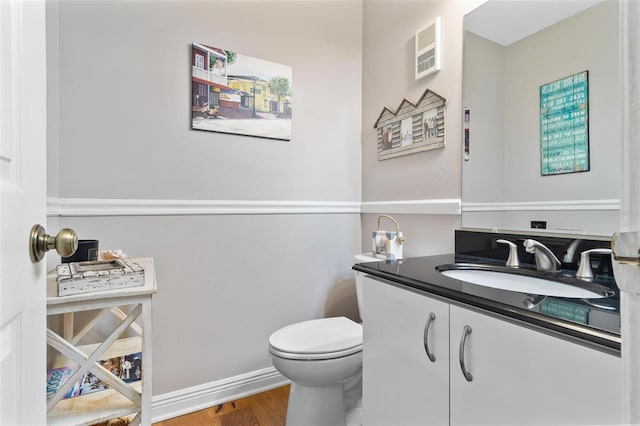 half bath featuring baseboards, vanity, toilet, and wood finished floors