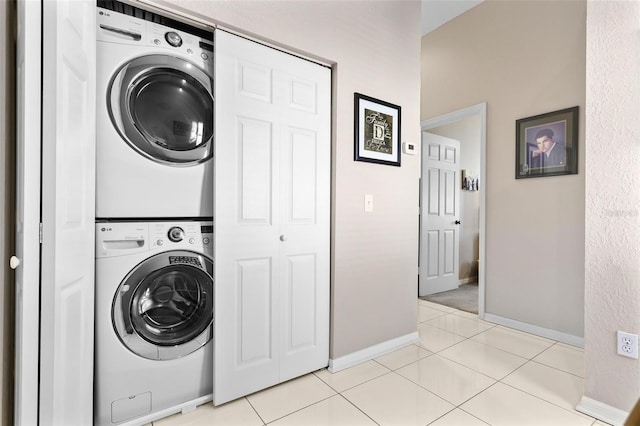 laundry area with stacked washer and dryer, laundry area, light tile patterned flooring, and baseboards