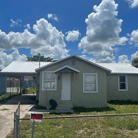 102 SE 6th Ave, Mulberry, FL 33860 - view of front of house with driveway, metal roof, fence, a carport, and stucco siding