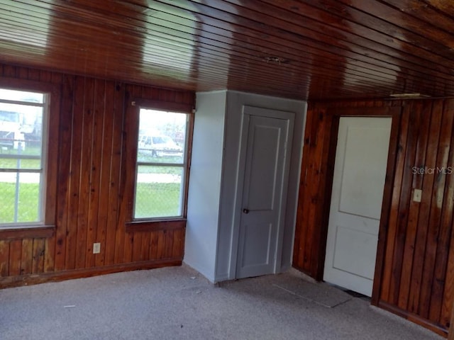 carpeted empty room with a healthy amount of sunlight, wood ceiling, and wooden walls