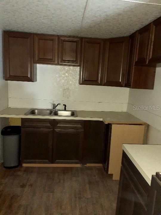 kitchen featuring a textured ceiling, light countertops, dark wood-type flooring, and a sink