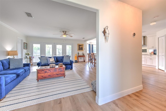 living room with visible vents, ornamental molding, a ceiling fan, light wood finished floors, and baseboards