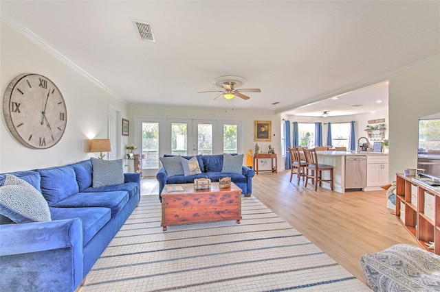 living room featuring visible vents, a ceiling fan, crown molding, and light wood finished floors