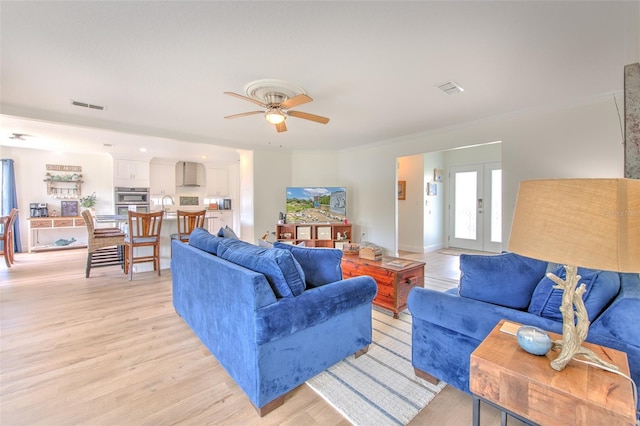 living room with a ceiling fan, visible vents, light wood-style floors, french doors, and crown molding