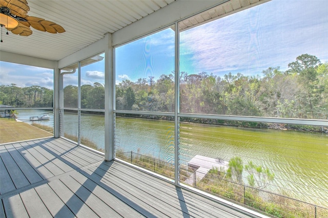 unfurnished sunroom with a ceiling fan, plenty of natural light, a forest view, and a water view