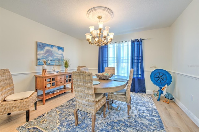 dining room featuring baseboards, a textured ceiling, an inviting chandelier, and light wood finished floors