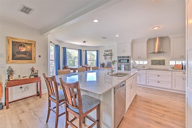 kitchen with wall chimney range hood, visible vents, a sink, stainless steel appliances, and a kitchen breakfast bar