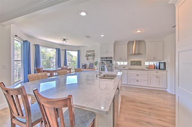 kitchen featuring white cabinetry, light wood-type flooring, wall chimney exhaust hood, and a sink