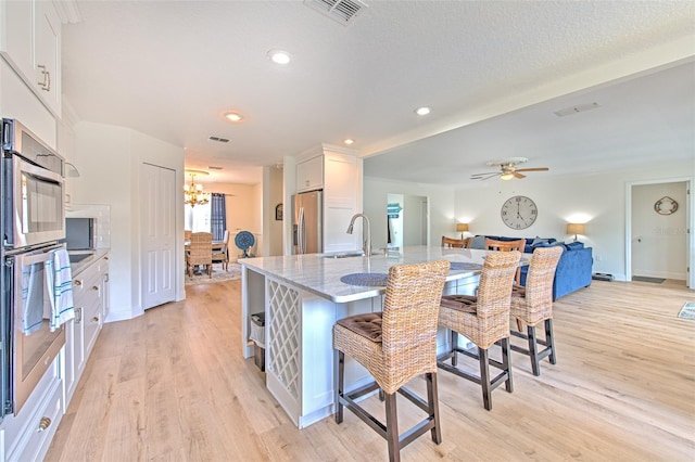 kitchen featuring visible vents, a sink, light stone counters, white cabinetry, and appliances with stainless steel finishes